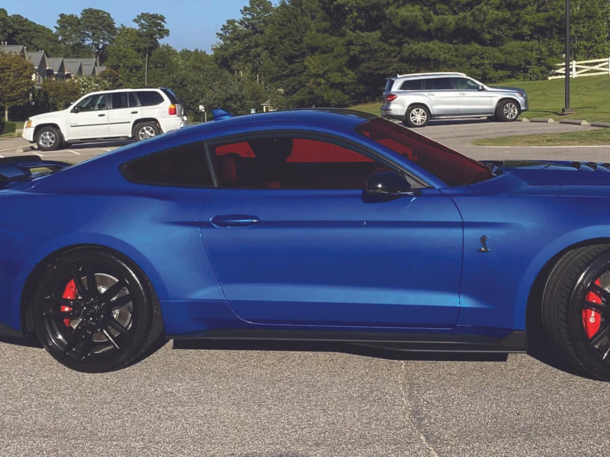 blue-mustang-car-with-red-window-tint A blue Ford Mustang sports car with black wheels and red window tint sitting in a parking lot.